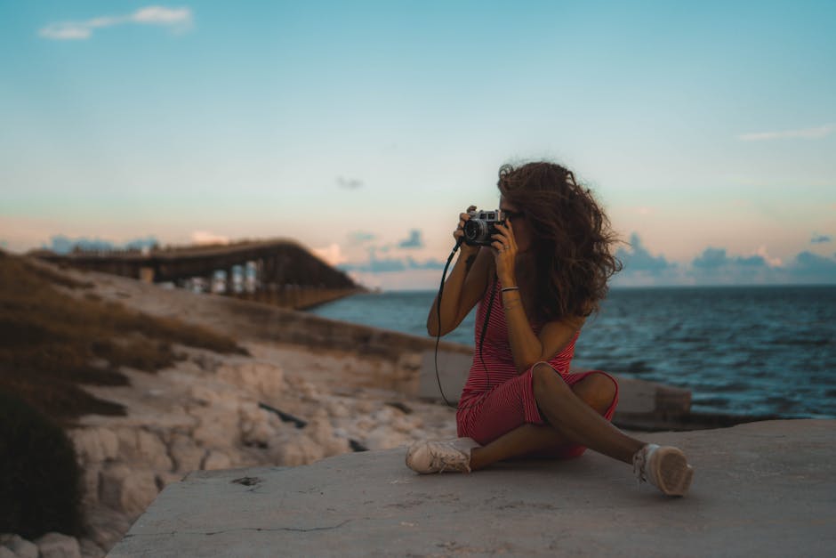A woman in a red dress taking photos by the seaside during sunset.
