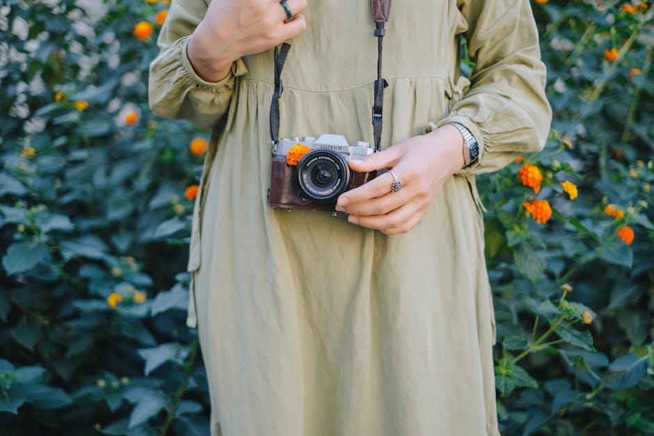 A woman in a casual green dress holds a vintage film camera in a blooming garden.