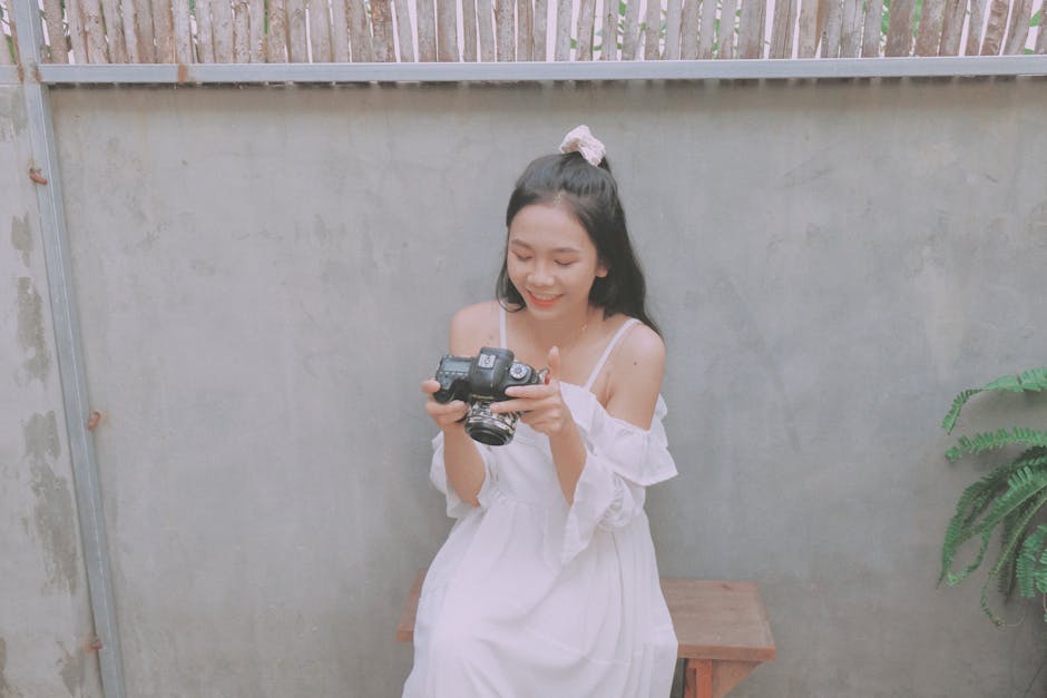 Happy woman in white dress holding a camera, sitting outdoors.